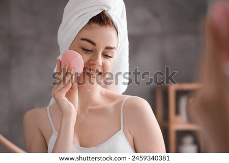 Washing face. Young woman with cleansing brush near mirror in bathroom