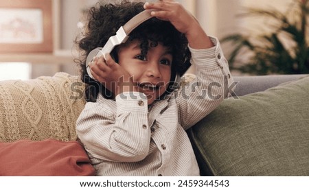 Child, headphones and happy on couch in home for relax, music and online streaming. Young boy, smile and listening to kids audio book, internet and radio in lounge in family house in Colombia