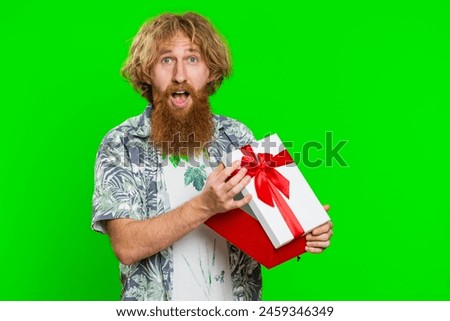 Happy caucasian man opening birthday gift box with red ribbon. Holidays surprise concept. Smiling redhead bearded guy receive great wrapped present celebrating isolated on green chroma key background