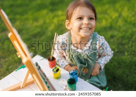 Little girl is painting a picture in the park on the green grass. Child development concept.