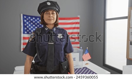 Hispanic policewoman standing confidently in a room with an american flag and ballot box, representing election security. Royalty-Free Stock Photo #2459360055