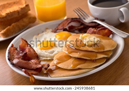 A delicious home style breakfast with crispy bacon, eggs, pancakes, toast, coffee, and orange juice. Royalty-Free Stock Photo #245938681