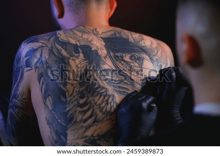 Shot of a tattoo artist hands forming perfect lines on man back with ink.