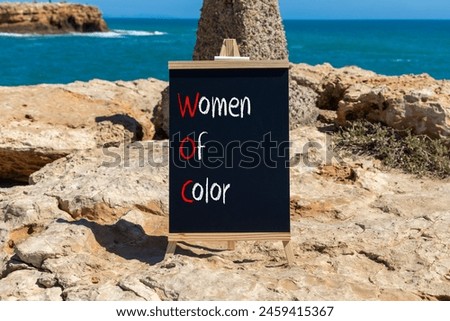 WOC women of color symbol. Concept words WOC women of color on beautiful yellow blackboard. Beautiful stone blue sky sea background. Business WOC women of color social issues concept. Copy space. Royalty-Free Stock Photo #2459415367