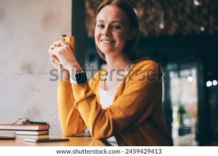 Portrait of cheerful woman feeling excited of photography hobby in cozy cafeteria recalls of beautiful moments, happy hipster girl looking at camera while holding vintage equipment in hands indoors