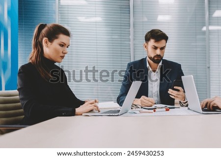Pensive two professionals searching information on laptops during working briefing at meeting table with boss of finance company.Proud CEO checking mail on smartphone collaborating with colleagues Royalty-Free Stock Photo #2459430253