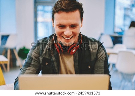 Excited hipster guy enjoying playing online games on laptop computer in coworking office with good wireless connection, happy young man laughing while watching movie on netbook during free time