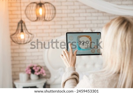 Young woman controlling home light with a digital tablet in the living room. Concept of a smart home and light control with mobile devices.