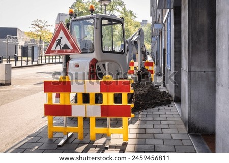 Excavator heavy duty machinery repairing the pavement in a city centre. Working sign and digging up soil from the sidewalk, roadwork repair with equipment in The Netherlands