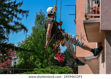 high-rise work on an apartment building. A construction worker inspects the condition of an apartment building for planned reconstruction using climbing equipment.