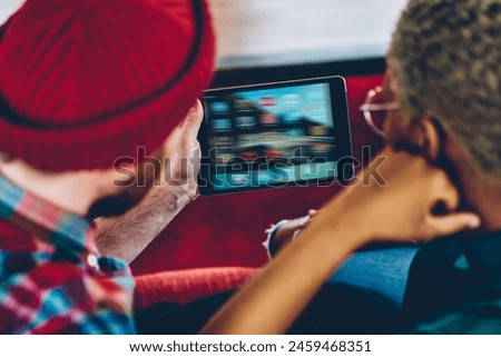 Cropped back view of young marriage watching movie online on modern tablet.Couple in love doing shopping on websites holding digital touch pad in hands and using wireless 4G internet connection