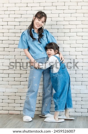 Happy asian beautiful young mother and cute daughter little girl smiling  posing standing on white brick wall background studio portrait Mother's Day love family parenthood childhood concept.