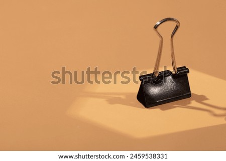 Conceptual clutch bag on brown background represented with paper clip. Spot light effect. Office bag concept. Royalty-Free Stock Photo #2459538331
