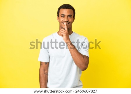 African American handsome man on isolated yellow background showing a sign of silence gesture putting finger in mouth