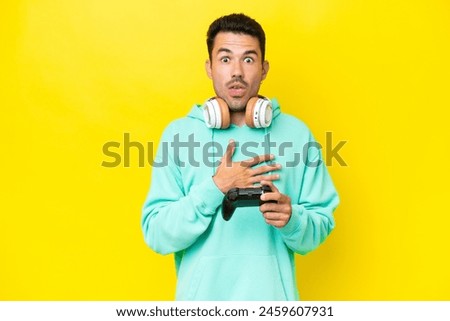 Young handsome man playing with a video game controller over isolated wall surprised and shocked while looking right