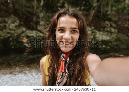 A selfie is a portrait of a young woman against the background of a forest area. The girl smiles at the camera. The concept of tourism, recreation