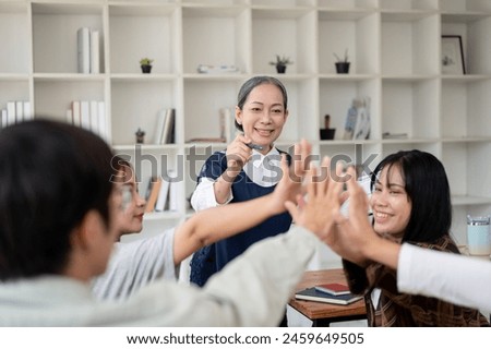 A group of cheerful Asian students putting their hands together in the classroom, brainstorming and cheering up. friendship, teamwork, education