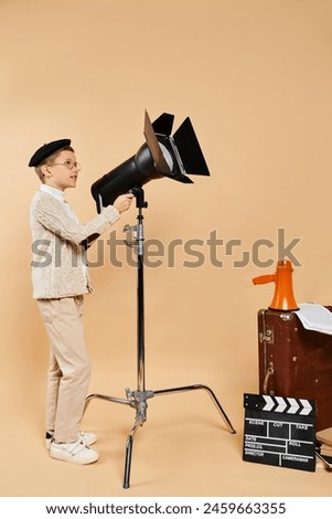 Preadolescent boy stands confidently next to camera and tripod.