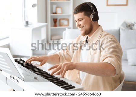 Young bearded man in headphones playing synthesizer at home Royalty-Free Stock Photo #2459664663