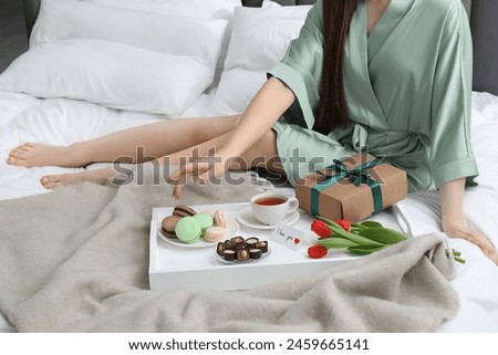 Tasty breakfast served in bed. Woman with desserts, tea, gift box, flowers and I Love You card at home, closeup