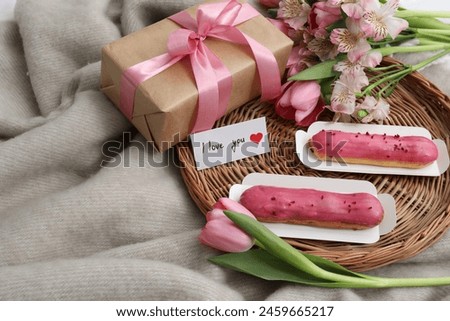 Tasty breakfast served in bed. Delicious eclairs, tea, flowers, gift box and card with phrase I Love You on blanket