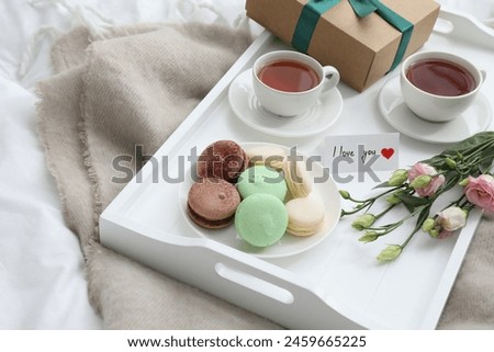 Tasty breakfast served in bed. Delicious macarons, tea, gift box, flowers and I Love You card on tray