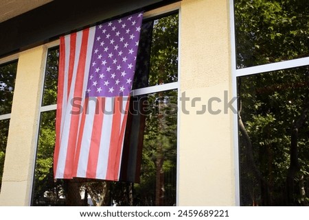 Street photo. American Stars and Stripes flag hangs on wall of yellow house with large picture windows. Facade. Concept of patriotism, presidential elections, independence day, 4th of july, USA. City
