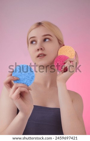 A beautiful woman holds face wash sponges on a pink background