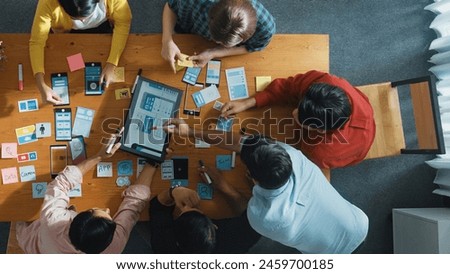 Top view of software developer team looking Ux Ui design for mobile phone interface from tablet while comparing and planning wireframe prototype designing together at creative workplace. Convocation.