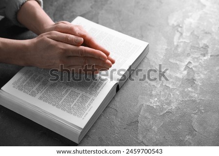 Religion. Christian woman praying over Bible at gray table, closeup. Space for text