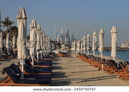 Long rows of sun loungers and folded umbrellas on the Dubai beach in the morning - overlooking the skyscrapers of Dubai Marina