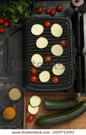 Electric grill with vegetables and spices on black marble table, flat lay