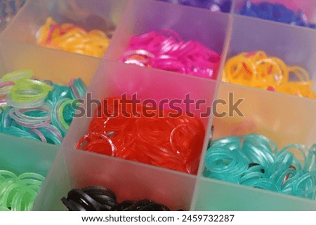 Vibrant loom bands in assorted hues stored in translucent plastic case. Close-up shots highlight vivid colors  complete set. Red, purple,  blue hues take center stage, enhancing visual appeal.