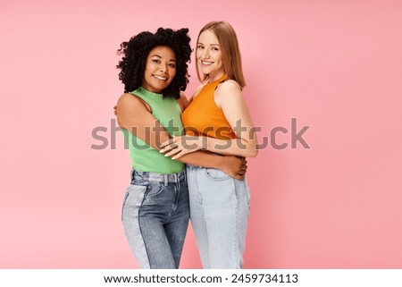Two attractive diverse women in cozy attire share a heartfelt hug in front of a pink backdrop. Royalty-Free Stock Photo #2459734113
