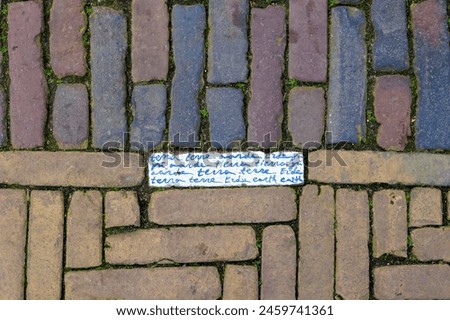 Brick pavement on the market square in the city of Delft in the Netherlands with an inscribed stone in which the word earth is written in Delft blue in many languages Royalty-Free Stock Photo #2459741361