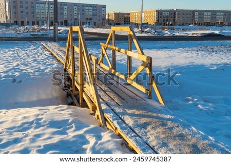 A wooden bridge over a snow covered ditch.