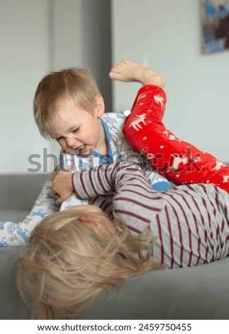 Two young children in pajamas are wrestling on the gray couch. They are playing and having fun. The boy's face shows aggression. They are wrestling each other. Brother and sister. Morning fun.