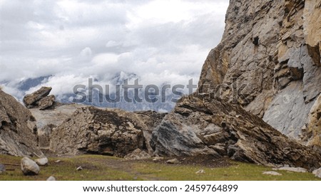  A panoramic landscape of the Himalayas Rocky mountains shrouded in a foggy and cloudy sky. Scattered stones lie across the green meadow in Gilgit-Baltistan,Pakistan.