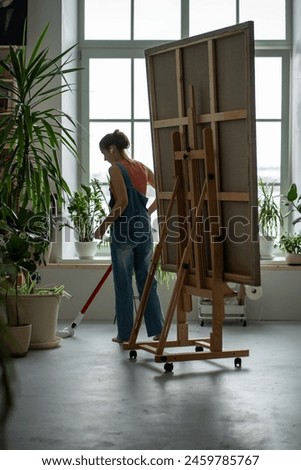 Female artist vacuuming workspace before, after work. Woman takes care of workspace, puts things in order in creative art studio, making comfortable clean environment setting up for productive work.
