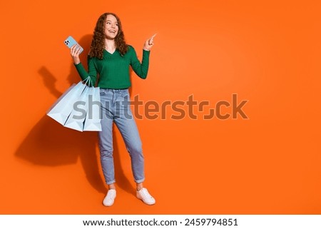 Photo of pretty excited lady dressed green shirt holding bargains texting device showing emtpy space isolated orange color background