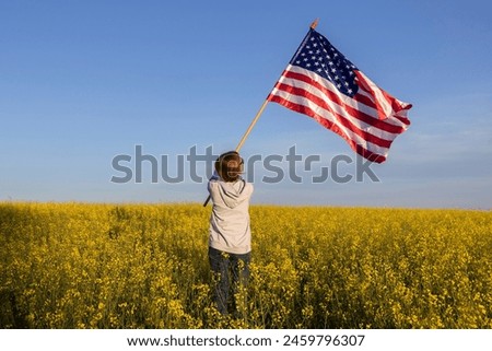 American flag is in hands of woman standing with back among blooming yellow rapeseed field. US Independence Day July 4th. Pride in one's homeland, freedom, patriotism, democracy. Travel around country