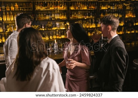 Men meet brunette women in nightclub and invite drink cocktails. Friends pay attention to bar counter with elite alcohol in club