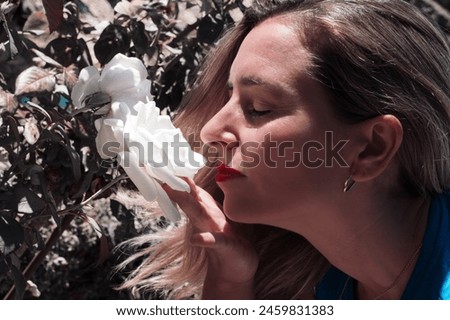 A woman is smelling a white flower. The woman is wearing a blue shirt