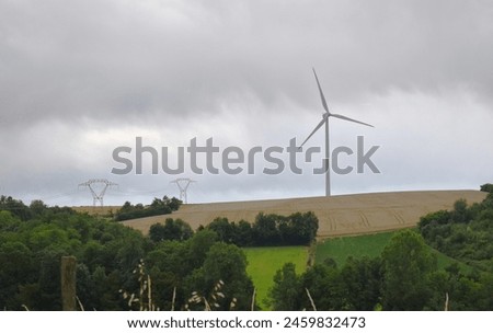 Rural landscape with a wind turbine erected in the middle of the fields. Electricity pylons in background. Royalty-Free Stock Photo #2459832473