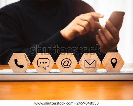 Contact us concept. Company website, FAQ, hotline phone number call, address, e-mail marketing and chat for customer support. Icons on hexagon wood blocks with businessman using mobile smart phone.
