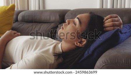 Image of moving clock over biracial woman laying on sofa. Lifestyle, fashion and light concept digitally generated image.