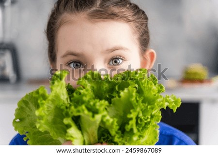 Portrait of a pretty little girl covering half of her face with fresh green lettuce leaves. Concept: healthy nutrition for children. High quality photo
