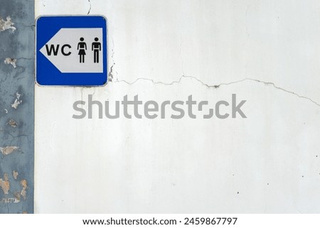 A simple blue and white sign indicating the location of public restrooms in a city. It shows clear, bold lettering with a classic symbol, such as a male and female icon, pointing in a direction.