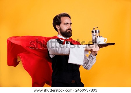 Elegant waiter with red cape carrying coffee on tray, having towel hanging over hand and posing as a superhero in studio. Young adult restaurant butler serving food and drinks.