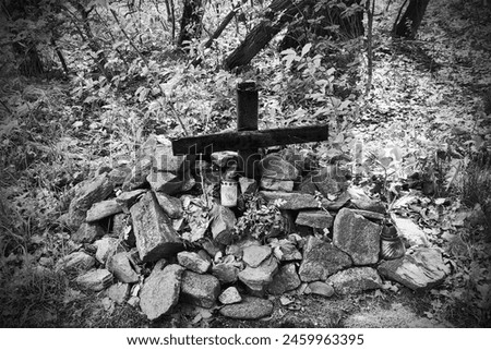 Cross in the ground and stones around it, memorial with a candle, object in nature, magical atmosphere, black and white photo